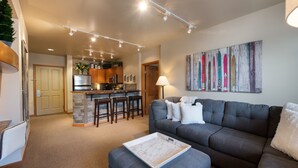 A modern living room with a grey sofa, a coffee table, and a kitchen in the background. - Zephyr Mountain Lodge, Condo | 2 Bedroom (Select-Rated Condo 2406) (Winter Park)