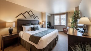 A hotel room with a large bed, two bedside tables with lamps, a desk with a chair, a potted plant, and a window with curtains. - Zephyr Mountain Lodge, Condo | 2 Bedroom (Select-Rated Condo 2406) (Winter Park)