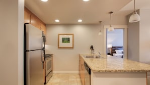 A modern kitchen with a refrigerator, oven, and dishwasher. There is a sink with a countertop and a framed picture on the wall.