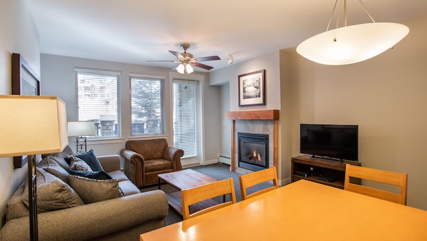 A living room with a sofa, chairs, a table, a fireplace, a TV, and a ceiling fan.