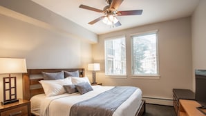 A neatly arranged bedroom with a bed, bedside tables, a ceiling fan, and windows.