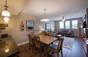 A dining area with a wooden table and chairs, a ceiling fan, and a sofa in the living room.