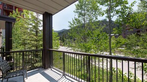 A balcony with a view of a road and trees, a table, and a chair. - Fraser Crossing/Founder Pointe, Townhome style Condo | Gondola Acess (Value-Rated Condo 3229) (Winter Park)