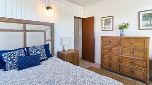 Une chambre à coucher comprenant un lit, une commode, une table de chevet et une lampe fixée au mur.