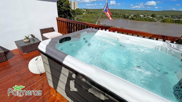 Un bain à remous sur une terrasse en bois, avec vue sur une rivière et des collines.