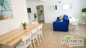 Un salon moderne avec une table à manger en bois, des chaises blanches, un canapé bleu et une petite plante.