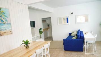 Un salon moderne avec une table à manger en bois, des chaises blanches, un canapé bleu et une petite plante.