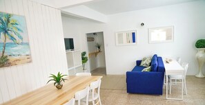 Ein modernes Wohnzimmer mit einem Holzespeisetisch, weißen Stühlen, einem blauen Sofa und einer kleinen Pflanze.