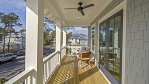 A covered porch with a ceiling fan, a wooden deck, and a view of the street and houses in the background. - Coastal Luxury on 30A: 4br/4ba: golf cart, walk to beach, shopping, & dining!   (Santa Rosa Beach)