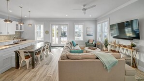 A spacious living area with a kitchen, dining space, and a TV mounted on the wall. - Coastal Luxury on 30A: 4br/4ba: golf cart, walk to beach, shopping, & dining!   (Santa Rosa Beach)