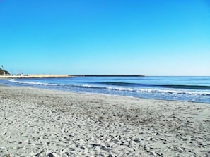 A sandy beach with gentle waves, a clear blue sky, and a distant pier.