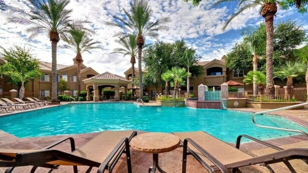 A swimming pool with lounge chairs and a small table, surrounded by palm trees and a building with a tiled roof. - Cozy 1-Bdrm Scottsdale Condo next to pool (Scottsdale)
