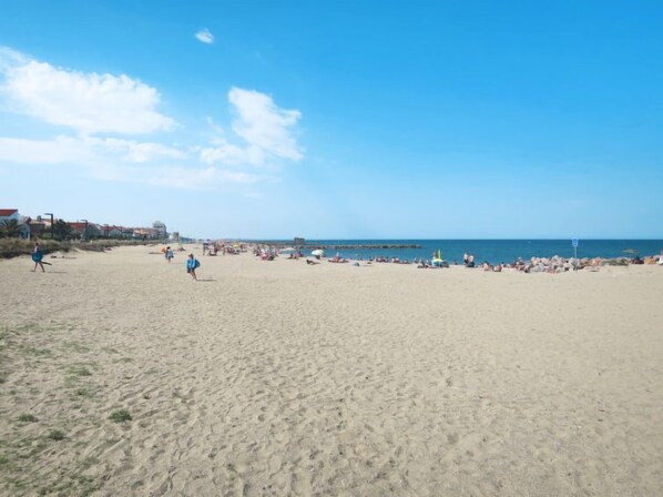 A wide sandy beach with people sunbathing and walking.