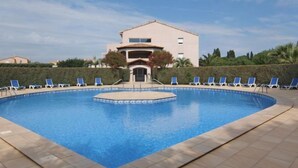 A swimming pool with blue water, surrounded by lounge chairs and a building in the background. - Les Reflets by Interhome (Saint Cyprien)