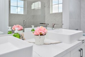 A modern bathroom with two sinks, a large mirror, and a potted plant.
