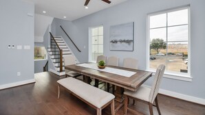 A dining area with a wooden table, chairs, a bench, a ceiling fan, a staircase, and a large window with a view of a parking lot. - New Luxury Stay mins from Downtown w/ dreamy common area (Houston)