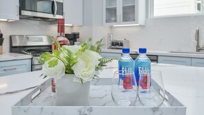 A marble tray with a vase of white flowers, two bottles of Fiji water, and an empty glass on a kitchen counter. - New Luxury Stay mins from Downtown w/ dreamy common area (Houston)