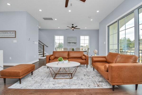 A spacious living room with a large window, a ceiling fan, and a sofa set.