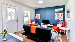 Een woonkamer met een donkerblauwe muur, een witte deur en een tv-meubel.