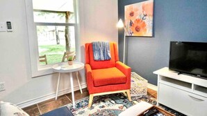 Een woonkamer met een rode fauteuil, een televisie, een bijzettafeltje met een plant en een groot raam.