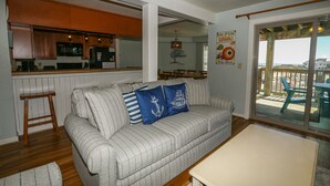 A living room with a sofa, a small table, and a view of the deck through glass doors. - IT'S A SHORE THING ☀️3BR Oceanfront Condo in Duck w/Community Pool☀️ (Duck)