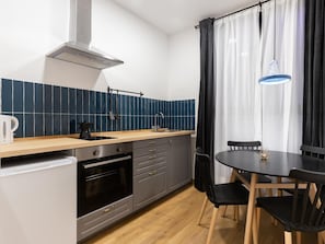 Een koelkast, een oven, kookgerei, borden en bestek, een eettafel