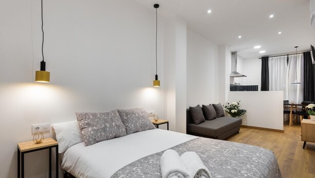 A modern bedroom with a large bed, bedside tables, a sofa, and a dining area.