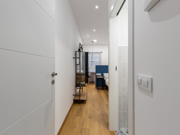A modern hotel corridor with white walls, wooden flooring, and a blue accent wall in the background.