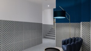 Ein modernes Zimmer mit Wandmustern, einer dunkelblauen Akzentwand, einem runden Tisch und einem blauen Sessel.