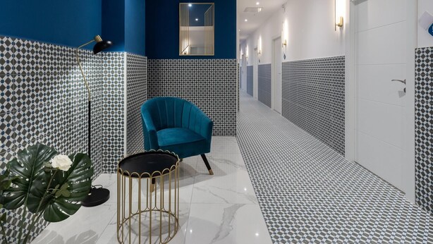 Un pasillo con paredes estampadas, un sillón azul, una mesita redonda y una planta en maceta.