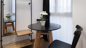 Una habitación pequeña con una mesa redonda negra, una silla negra, un taburete de madera y una planta en maceta con flores blancas.
