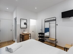 Une chambre d’hôtel moderne avec un grand lit, une table de chevet en bois, un lavabo blanc, un miroir et un téléviseur fixé au mur.