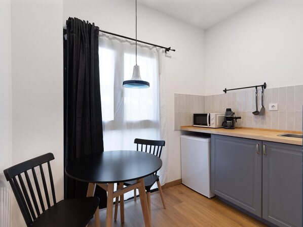 Une cuisine compacte comprenant une table à manger, des chaises, un four à micro-ondes, une machine à café et un petit réfrigérateur.