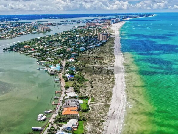 An aerial view of a coastal area with a beach, residential buildings, and a marina.