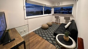 A modern living room with a black sofa, two armchairs, a small round table with a plant, and a TV on a wooden table. - Your Perfect Retreat with Unlimited WiFi, Netflix,Steps Away from Beach & Shops  (Rosebud)