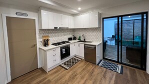A modern kitchen with white cabinets, a gas stove, and a dishwasher. There is a door labeled "Bathroom" and a sliding glass door leading to an outdoor area. - Your Perfect Retreat with Unlimited WiFi, Netflix,Steps Away from Beach & Shops  (Rosebud)
