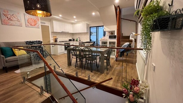 A modern kitchen with white cabinets, a dining area with a glass railing, and a staircase with wooden railings. - Your Perfect Retreat with Unlimited WiFi, Netflix,Steps Away from Beach & Shops  (Rosebud)