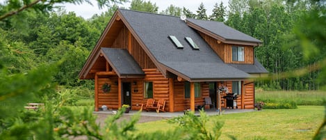 A log cabin with a sloped roof, a porch with a chair, and a small outdoor seating area.