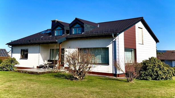 Ein zweistöckiges Haus mit geneigtem Dach, einer Veranda und einem kleinen Vorgarten.