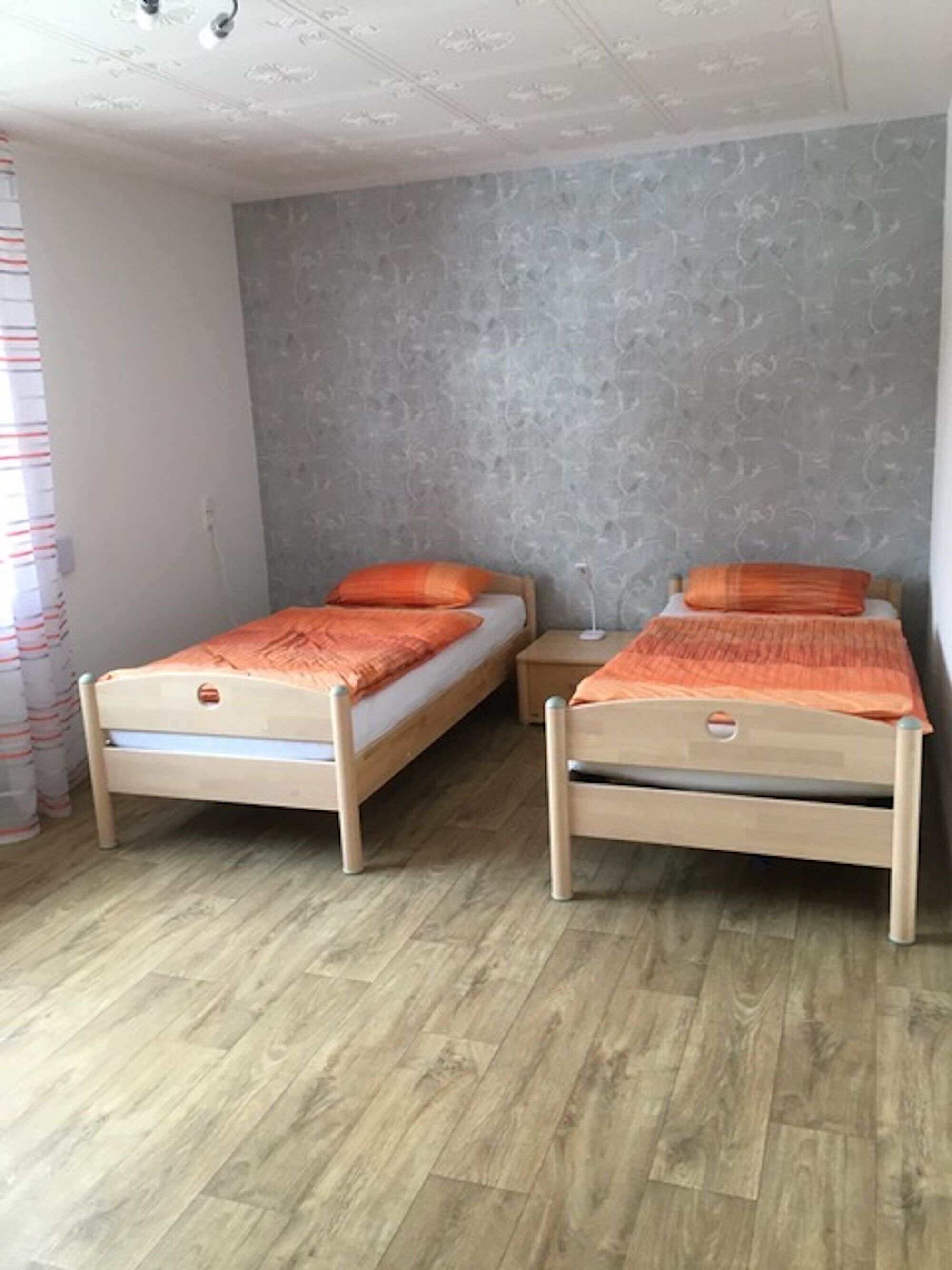 A room with two wooden beds, a grey textured wall, and a wooden floor.
