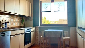 Eine Küche mit Fliesenboden, weißen Schränken, einem Tisch mit Stühlen und einem Fenster mit Aussicht.