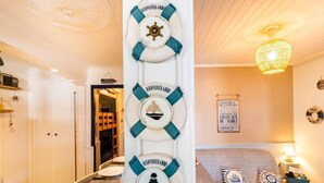 Ein Zimmer mit vertikal angeordneten Rettungsvorrichtungen, einem Bett mit maritime Kissen und einem an der Wand befestigten Schild.