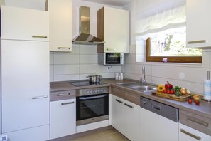 Une cuisine moderne avec des meubles blancs, un four encastré, un micro-ondes et une fenêtre donnant sur un espace verdoyant.