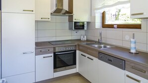 A modern kitchen with white cabinetry, a built-in oven, a microwave, and a window with a view of greenery.