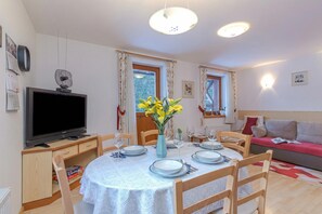 Ein Essbereich mit einem runden Tisch, Stühlen, einem Fernseher und einer Vase mit Blumen.