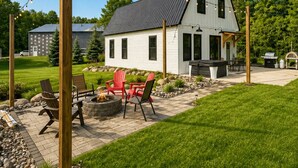 Een wit huis met een zwart dak, een vuurkorf en zitplaatsen buiten.