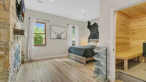 Een slaapkamer met een stenen muur, een bed, een raam met gordijnen, een kunstwerk aan de wand en een houten bank.