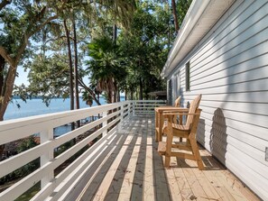 A wooden deck with a white railing, overlooking a body of water, with a house on the right.