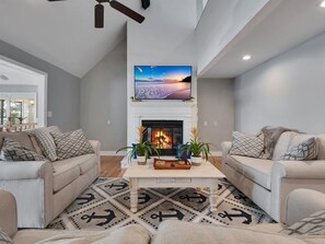 A living room with a fireplace, two sofas, a coffee table, and a TV mounted above the fireplace.