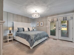 Une chambre à coucher avec un lit, des tables de chevet, un lustre et une porte donnant sur une vue agréable.